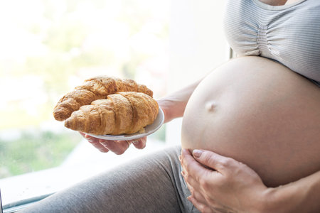 A pregnant woman with belly holding a plate of croissants. The concept weight control and an...