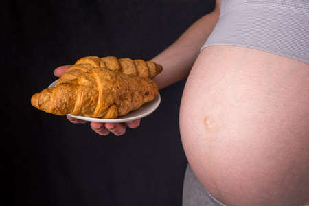 A pregnant woman with belly holding a plate of croissants. The concept weight control and an unhealthy diet during pregnancyの写真素材