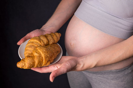 A pregnant woman with belly holding a plate of croissants. The concept weight control and an...