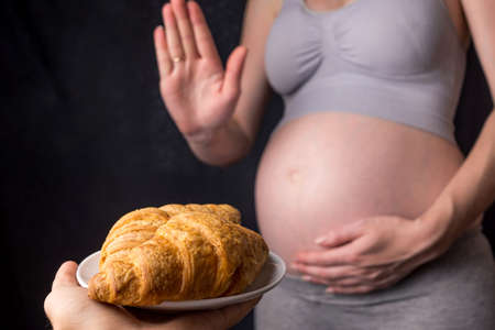 A pregnant woman with belly refuses to croissants. The concept weight control and an unhealthy diet during pregnancyの写真素材