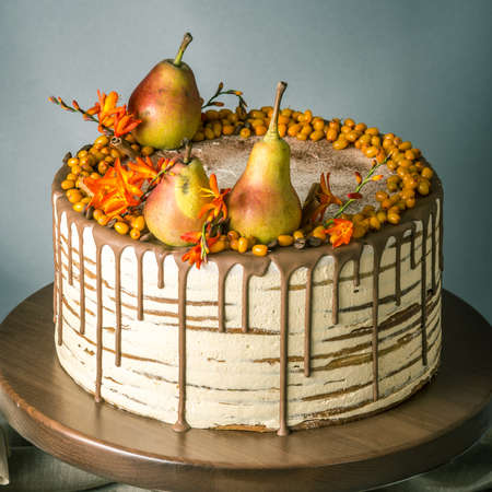 Beautiful large honey cake pour over the chocolate and decorated on top with pears and sea buckthorn on a wooden table. The concept of sweet autumn still lifeの写真素材