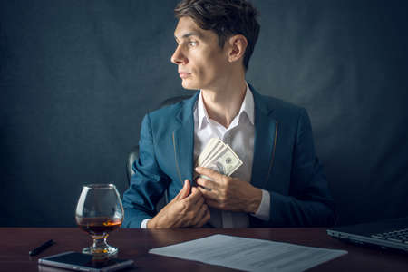 Man Businessman in suit puts money in his pocket. A bribe in the form of dollar bills. The concept of corruption and briberyの写真素材