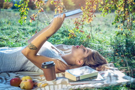 Attractive woman reading an interesting book lying in the Park on a green lawn on a Sunny summer...