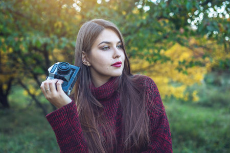 Beautiful woman in autumn Park holds vintage retro camera. The concept of photography as a hobby