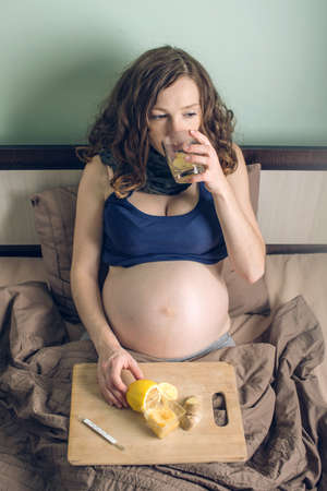 Pregnant woman lying in bed sick with colds and flu. The woman treated with lemon ginger tea and honey.の写真素材