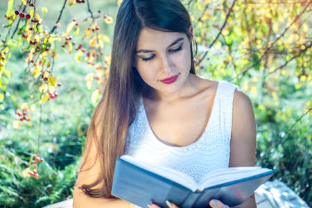 Attractive woman reading an interesting book sitting in a Park on a green lawn on a Sunny summer day. The concept of student educationの写真素材