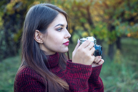 Beautiful woman in autumn Park holds vintage retro camera. The concept of photography as a hobby