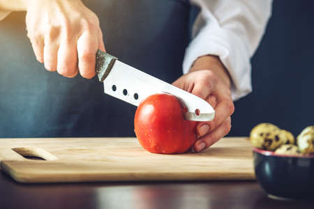 The chef in black apron cuts vegetables. The concept of eco-friendly products for cookingの写真素材