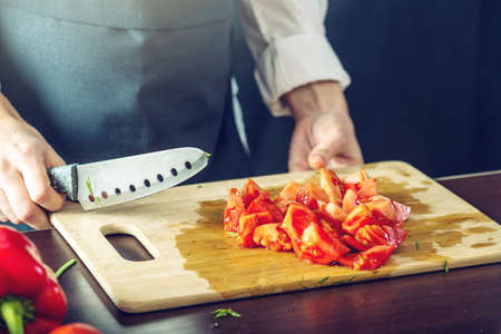 The chef in black apron cut the tomatoes. The concept of eco-friendly products for cookingの写真素材