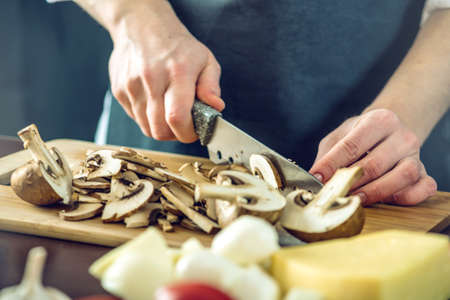 The chef in black apron cuts mushrooms with a knife. The concept of eco-friendly products for cookingの写真素材
