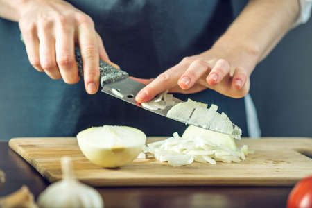 The chef in black apron cuts an onion with a knife. The concept of eco-friendly products for cookingの写真素材