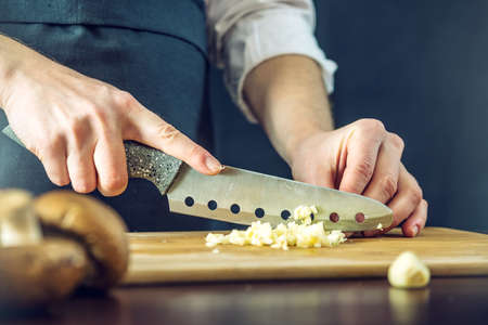 The chef in black apron cuts the garlic with a knife. The concept of eco-friendly products for cookingの写真素材