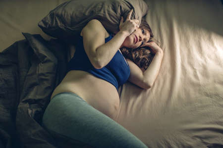 Pregnant woman feeling pain in her belly lying in bed with insomnia at night. The concept of pregnancy and healthの写真素材