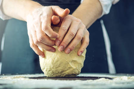 The chef in black apron makes pizza dough with your hands on the table. The dark backgroundの写真素材