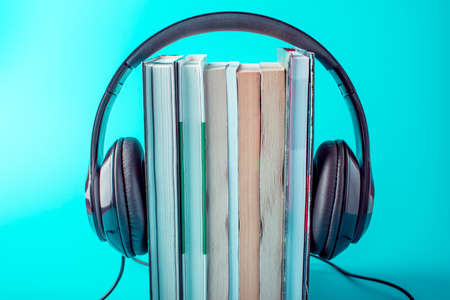 Black headphones with a stack of books on a blue background. The concept of audiobooks and modern educationの写真素材