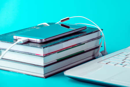 Phone with white earphones next to a stack of books on a blue background. The concept of audiobooks and modern educationの写真素材