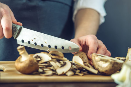 The chef in black apron cuts mushrooms with a knife. The concept of eco-friendly products for...