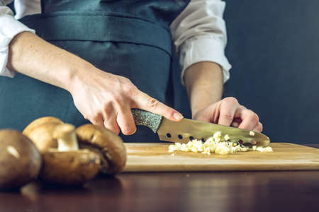 The chef in black apron cuts the garlic with a knife. The concept of eco-friendly products for cookingの写真素材