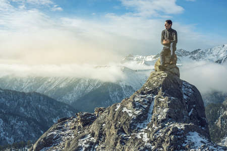 A young man in a sweater with phone in hand on the top of a snowy mountain far from civilization on a background of blue sky. The concept of activity and the availability of mobile connectionの写真素材