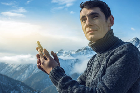 A young man in a sweater with phone in hand on the top of a snowy mountain far from civilization on...
