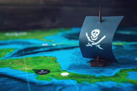 Toy boat pirate flag skull and bones on the world map of the playing field handmade Board games. The concept of piracyの写真素材