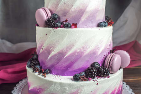 Beautiful delicious three-tiered wedding cake decorated with berries blueberry and blackberries in pink purple color. The concept of a festive dessertの写真素材