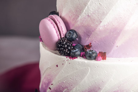 Beautiful delicious three-tiered wedding cake decorated with berries blueberry and blackberries in pink purple color. The concept of a festive dessertの写真素材