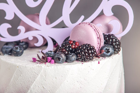 Beautiful delicious three-tiered wedding cake decorated with berries blueberry and blackberries in pink purple color. The concept of a festive dessertの写真素材