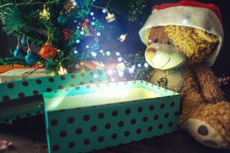 A Teddy bear opens a gift on background glowing Christmas tree. The concept of new year's eve Magic