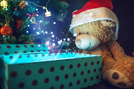 A Teddy bear opens a gift on background glowing Christmas tree. The concept of new year's eve Magicの写真素材