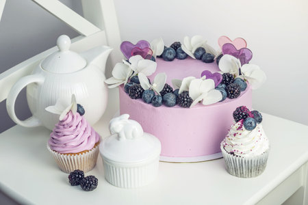 Purple beautiful cake decorated with berries, blackberries and blueberries on top with cupcakes on the festive table.の写真素材