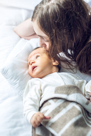 Happy caring mother holding a smiling baby boy and kisses him in the bedroom. The concept of the...