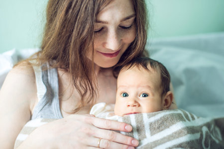 Happy caring mother holding baby boy in the bedroom. The concept of the tenderness of motherhood and...