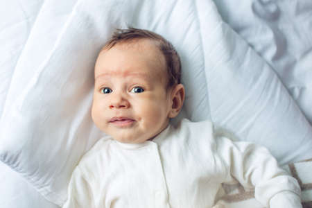 Cute funny baby lying on a white bed covered with a blanket. The concept of The tenderness of motherhood and family valuesの写真素材