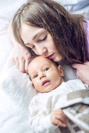 Happy caring mother holding baby boy in the bedroom. The concept of the tenderness of motherhood and family valuesの写真素材