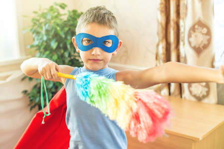 Boy child superhero costume playing is cleaning the house. The concept of children helping their parents in the form of a gameの写真素材