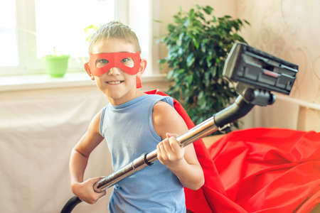 Boy child superhero costume playing is cleaning the house. The concept of children helping their parents in the form of a gameの写真素材