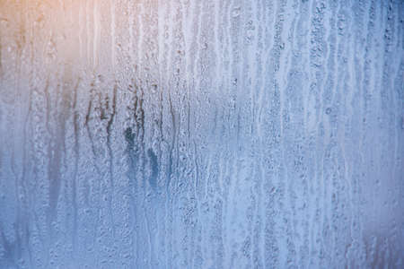 The morning sunrise through the raindrops on the glass. Condensation on Windows in winter. The texture of the water abstractionの写真素材