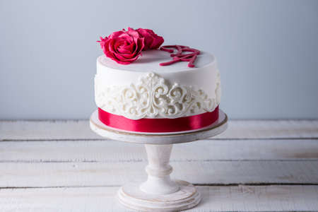 Beautiful white wedding cake decorated with flowers red roses and ribbon. The concept of elegant holiday dessertsの写真素材