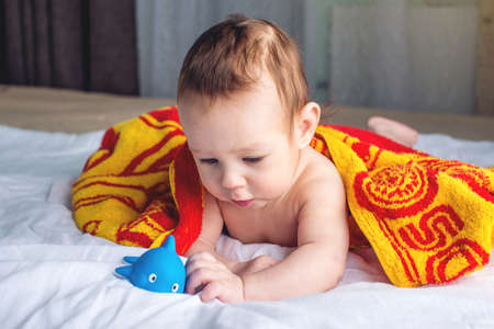 Beautiful happy baby with blue eyes lying on a blanket with a duck wrapped in a towel after bathingの写真素材