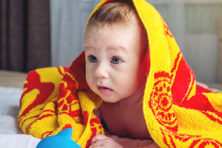 Beautiful happy baby with blue eyes lying on a blanket with a duck wrapped in a towel after bathingの写真素材