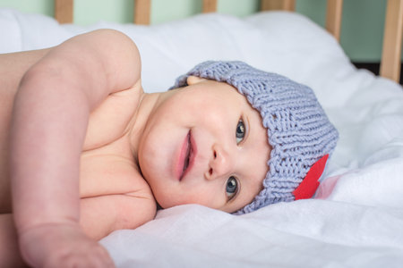 A beautiful happy baby is lying in a crib on a blanket in a knitted beanie with a heart. The concept...