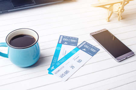 Cup of coffee plane tickets, phone and laptop on white wooden background. The concept of buying the online ticket booking for travelの写真素材