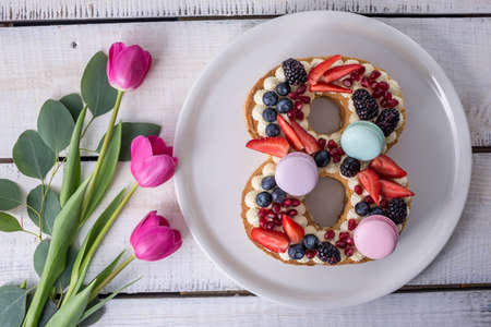 Homemade cake in shape of number 8 decorated with white cream and berries and flowers tulips. Sweet dessert as a gift for women's day on the eighth of Marchの写真素材