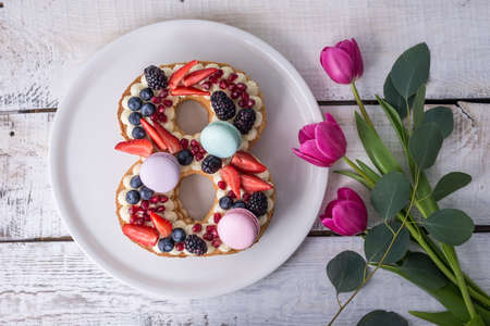 Homemade cake in shape of number 8 decorated with white cream and berries and flowers tulips. Sweet dessert as a gift for women's day on the eighth of Marchの写真素材