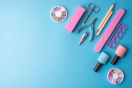 A set of cosmetic tools for manicure and pedicure on a blue background. Gel polishes, nail files and clippers, and the lamp top viewの写真素材