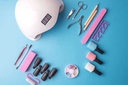 A set of cosmetic tools for manicure and pedicure on a blue background. Gel polishes, nail files and clippers, and the lamp top viewの写真素材