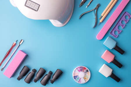 A set of cosmetic tools for manicure and pedicure on a blue background. Gel polishes, nail files and clippers, and the lamp top viewの写真素材