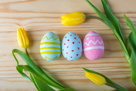 Colorful bright Easter eggs with yellow Tulip hand painted on a light wooden background. Festive...