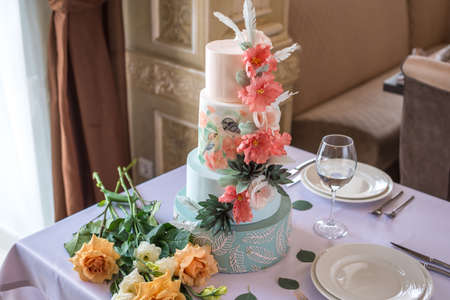 A beautiful home wedding for-tiered cake on the table in the restaurant decorated with pink roses and green leaves in a rustic style. celebratory Banquetの写真素材